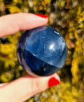 Close up of polished blue fluorite sphere showing natural banding and internal crystal structure, deep blue tones with slight translucency, high polish finish, round fluorite crystal ball, perfect for collectors, crystal display, metaphysical use, and home decor, photographed outdoors in natural light.
