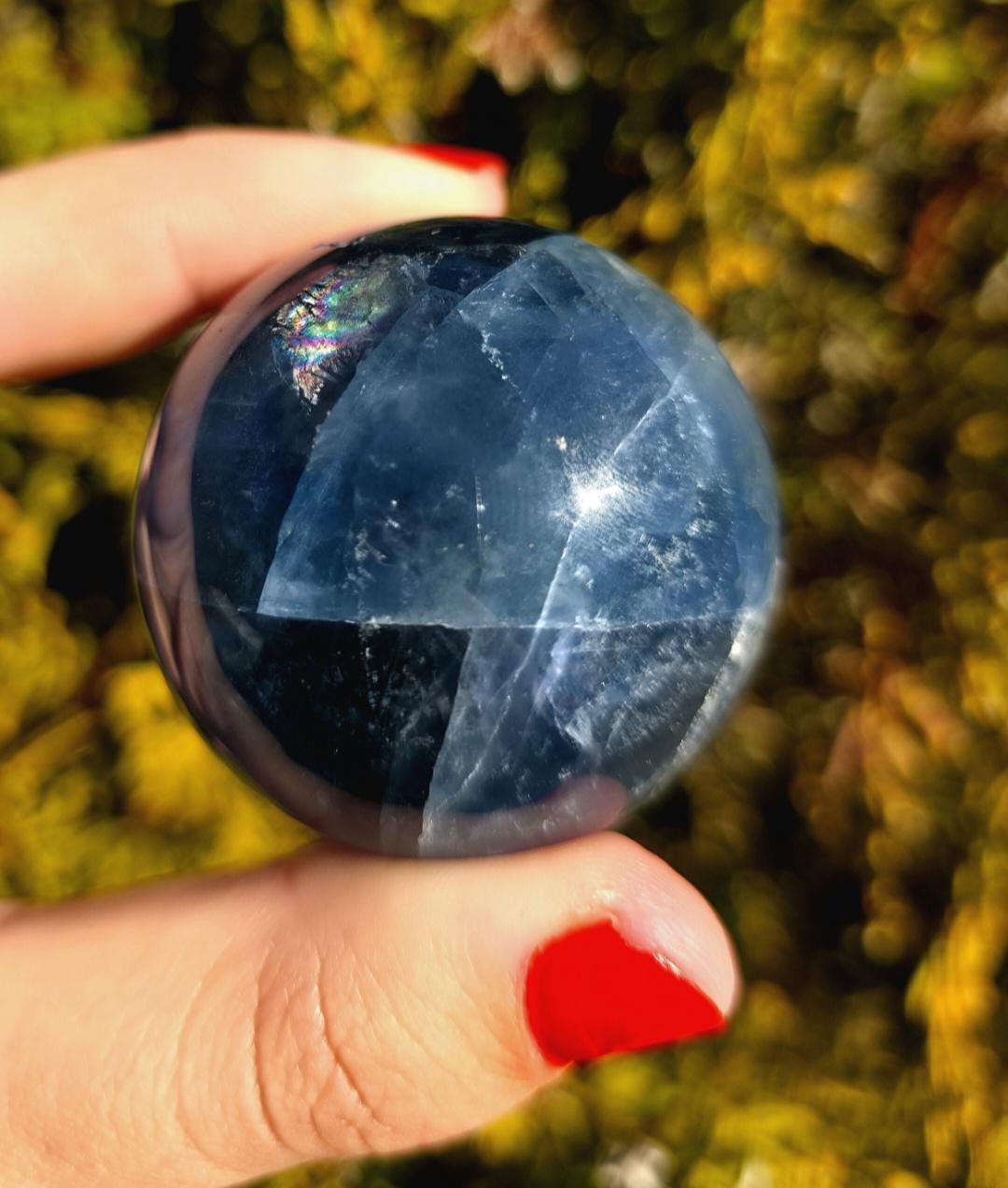 Close up of polished blue fluorite sphere showing natural banding and internal crystal structure, deep blue tones with slight translucency, high polish finish, round fluorite crystal ball, perfect for collectors, crystal display, metaphysical use, and home decor, photographed outdoors in natural light