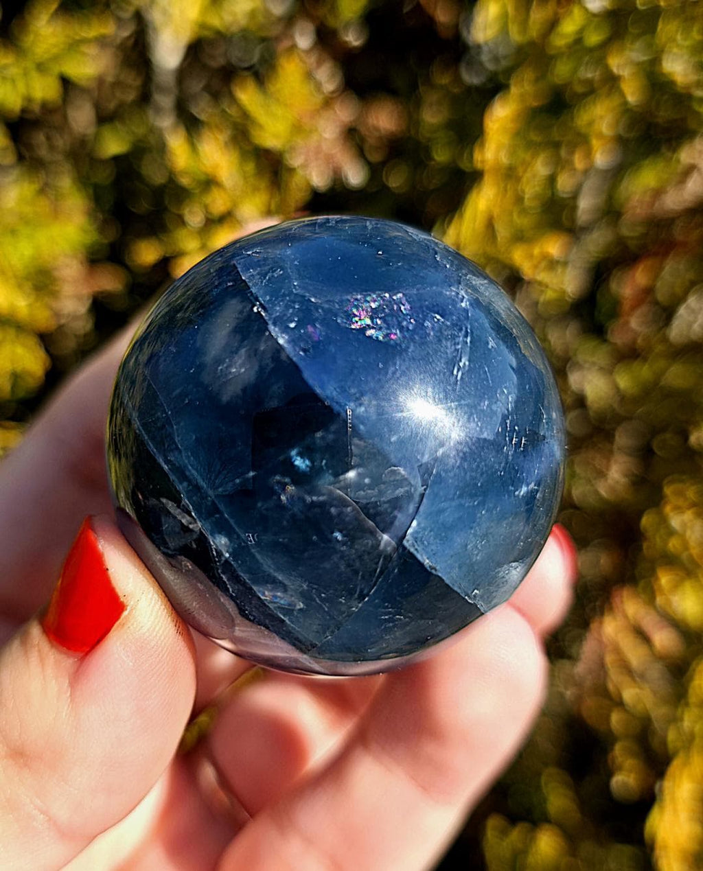 Close up of polished blue fluorite sphere showing natural banding and internal crystal structure, deep blue tones with slight translucency, high polish finish, round fluorite crystal ball, perfect for collectors, crystal display, metaphysical use, and home decor, photographed outdoors in natural light