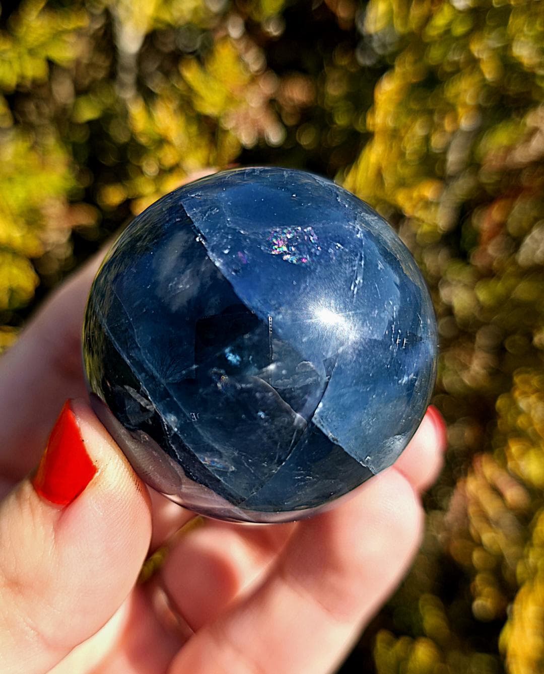 Close up of polished blue fluorite sphere showing natural banding and internal crystal structure, deep blue tones with slight translucency, high polish finish, round fluorite crystal ball, perfect for collectors, crystal display, metaphysical use, and home decor, photographed outdoors in natural light