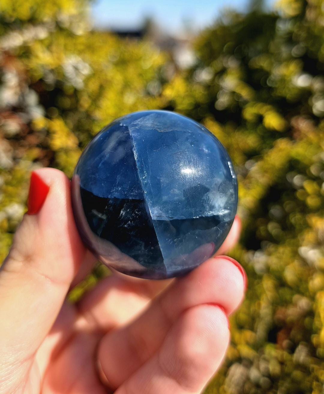 Close up of polished blue fluorite sphere showing natural banding and internal crystal structure, deep blue tones with slight translucency, high polish finish, round fluorite crystal ball, perfect for collectors, crystal display, metaphysical use, and home decor, photographed outdoors in natural light